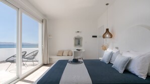 A bedroom with a large bed, a view of the sea, and a balcony with chairs. - Manios Suites (Naxos)