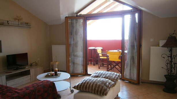 A cozy living room with a TV, a small table with candles, a sofa, and a sliding glass door leading to an outdoor seating area. - Sea View Athina's Home (Kefalonia)