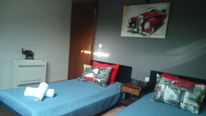 A hotel room with two beds, a nightstand, a lamp, a heater, and a painting on the wall. - Sea View Athina's Home (Kefalonia)