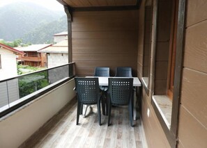 Ein Balkon mit Tisch und Stühlen, Holzboden und Blick auf Gebäude und Berge.