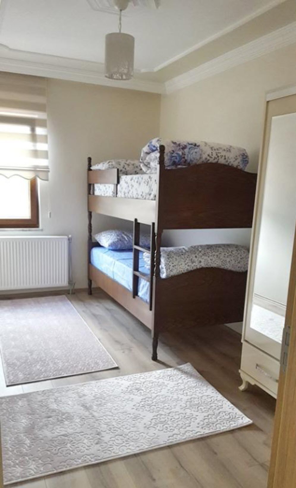 Une chambre avec un lit superposé, un radiateur, un tapis à motifs et une armoire.