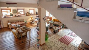 Un'ampia zona giorno con pavimento in legno, un divano, un tavolino da caffè e una scala che conduce a un pianerottolo con libri.