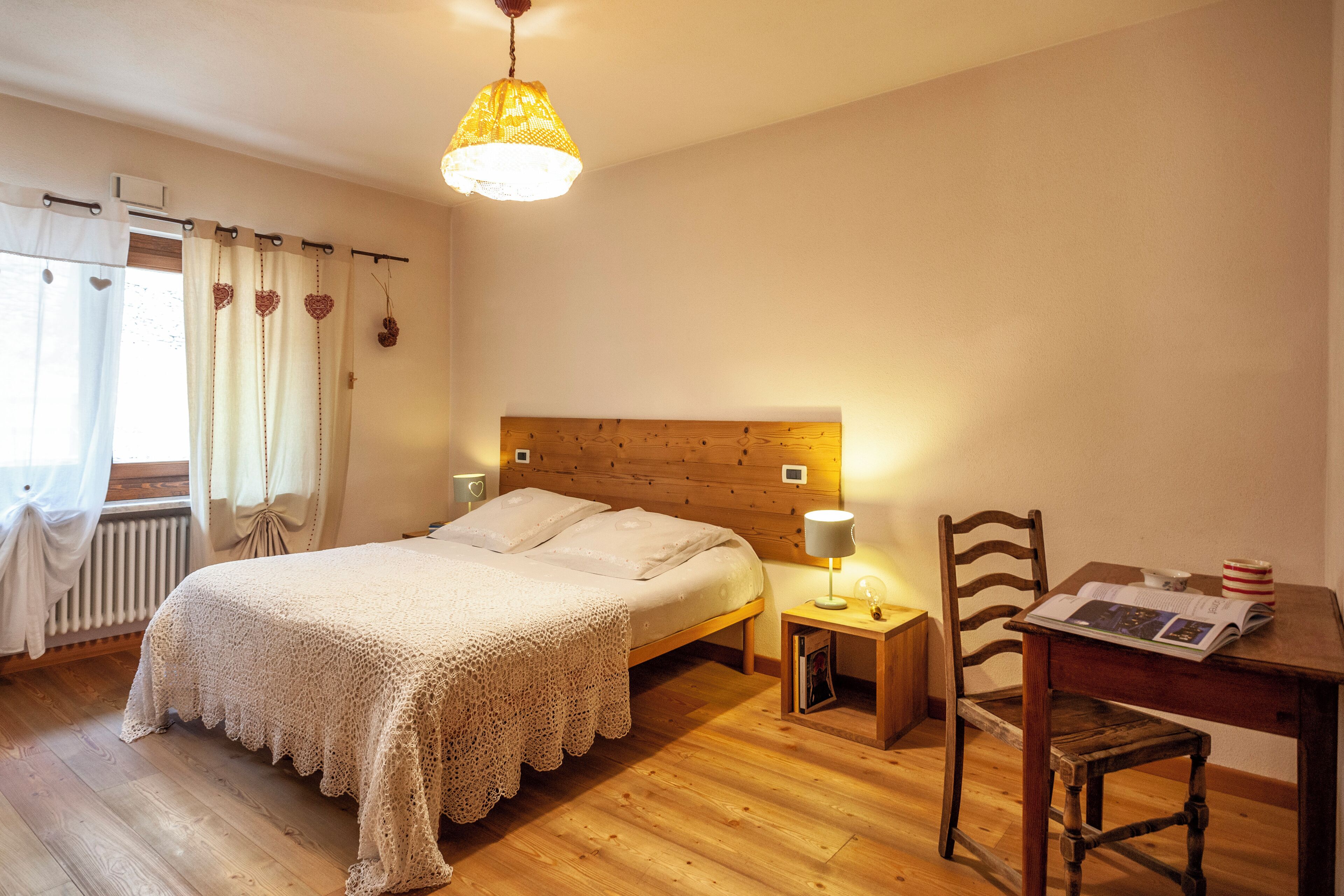 A bedroom with a wooden headboard, a bed with a white blanket, a bedside table with a lamp, and a chair with a magazine.