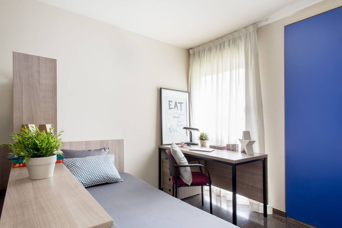 A modern bedroom with a bed, a desk, and a potted plant.