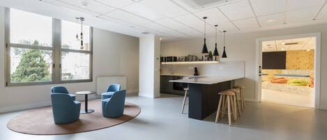 Una cocina moderna con barra, ventanas amplias y una zona de estar con sillas azules.