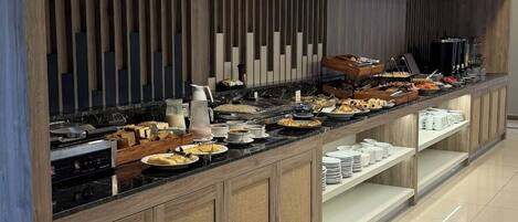 A buffet setup with a variety of food items, a coffee station, and a seating area with a view of the sky.