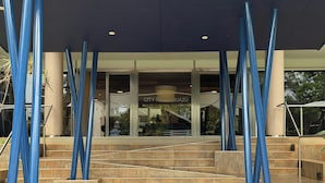 A modern building entrance with a glass facade, a staircase leading up to a door, and blue vertical elements. - City Falls Iguazú (Puerto Iguazú)