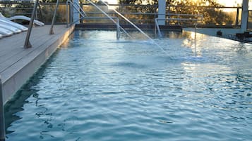 A swimming pool with a metal ladder and steps, surrounded by a deck area.
