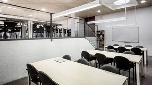 Uma sala de aula moderna com paredes de tijolo branco, cadeiras pretas e mesas de madeira.