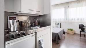 Uma cozinha moderna com armários brancos, fogão e pia. Há uma área de jantar com mesa e cadeiras, e uma janela com cortinas leves.