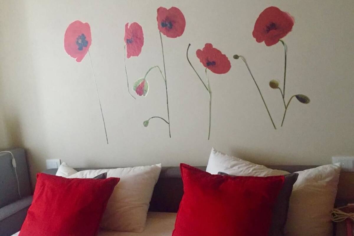 A bedroom with a bed, red and white pillows, and a wall with painted flowers.