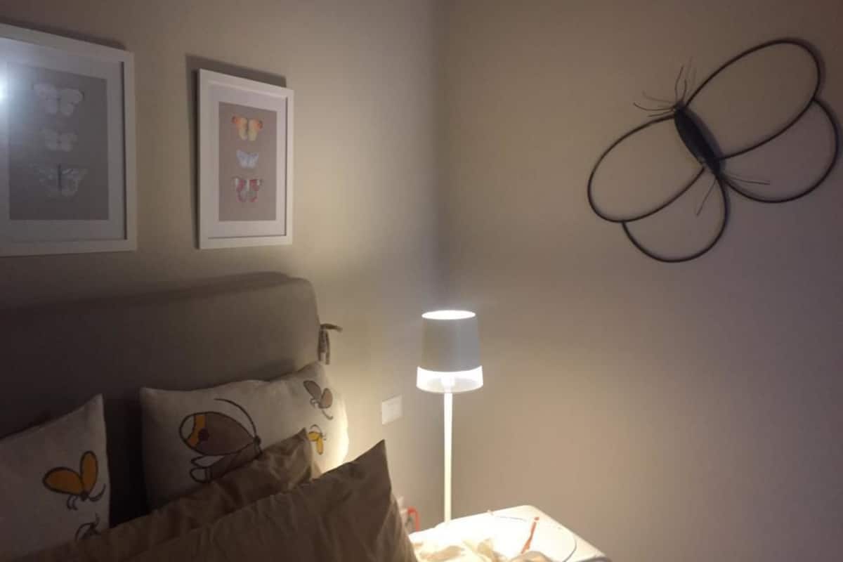A bedroom with a bed, pillows, a wall-mounted lamp, and butterfly decorations.