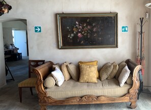 Um sofá de madeira com várias almofadas, um quadro floral emoldurado na parede e placas de sinalização.