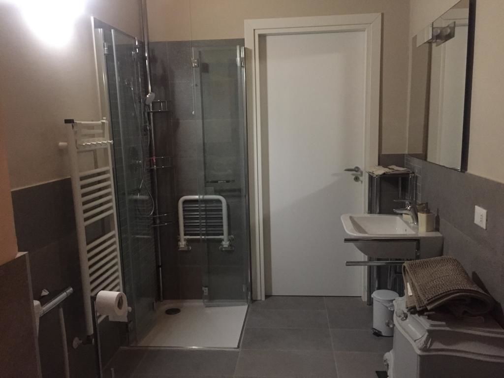 A bathroom with a glass-enclosed shower, a white door, a sink with a mirror, and a towel rack.