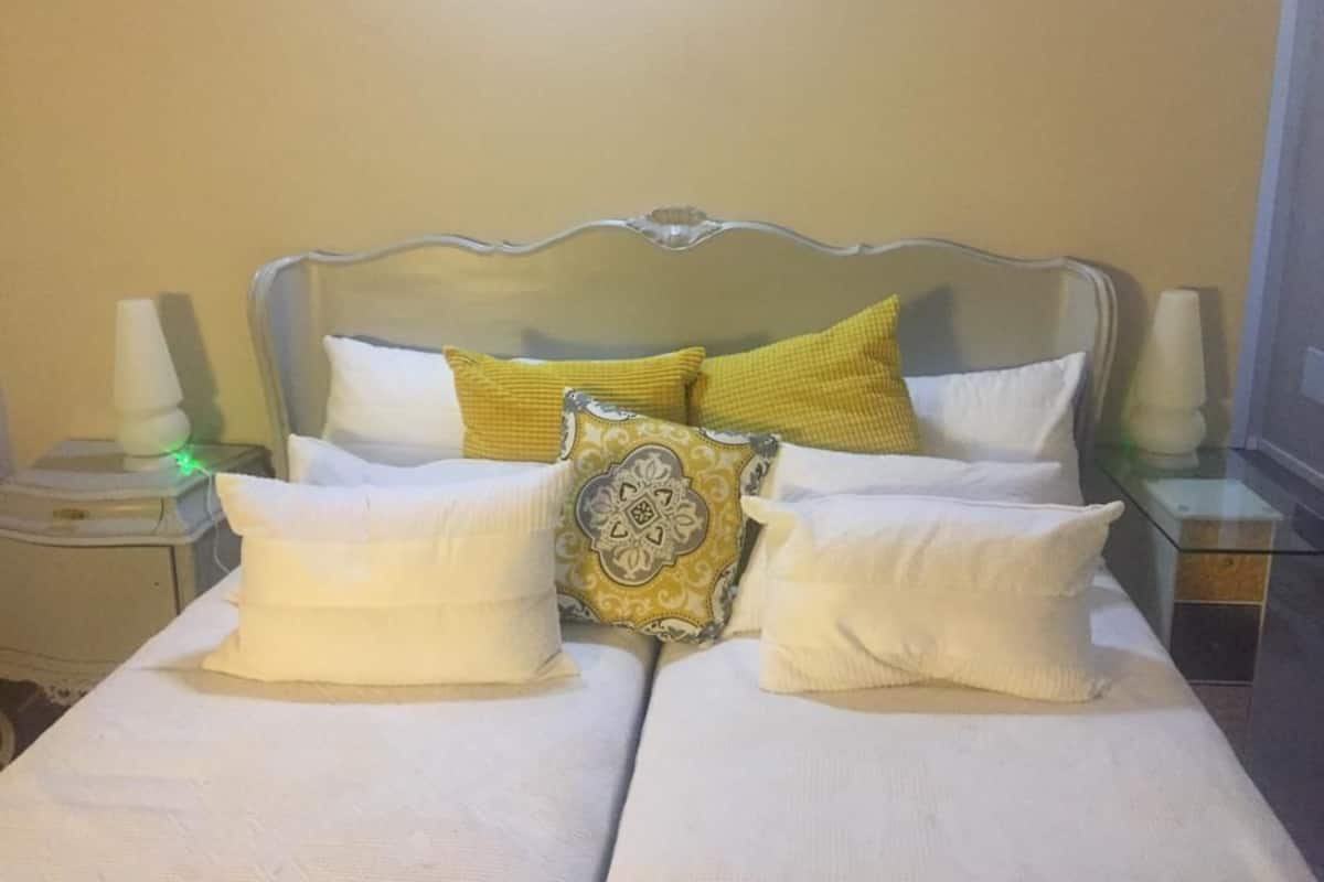 A double bed with white bedding and decorative pillows, a glass headboard, bedside tables with lamps, and a plain wall.