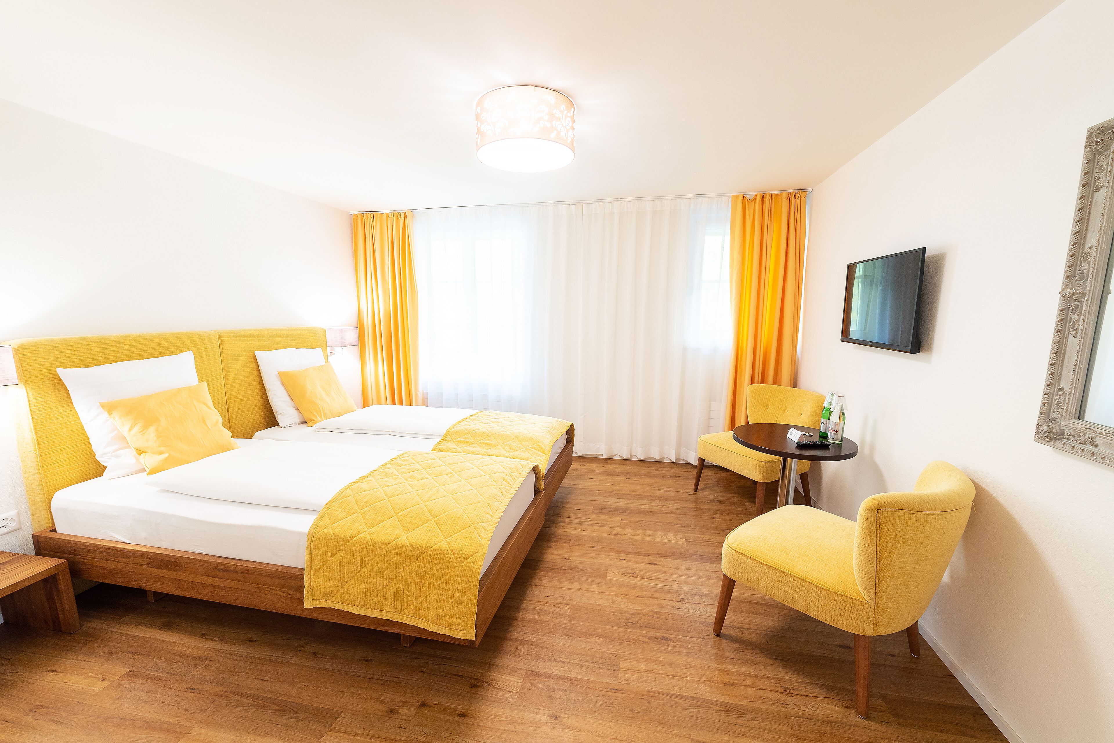 Ein Hotelzimmer mit Doppelbett, einem kleinen Tisch mit Stuhl und einem an der Wand montierten Fernseher.