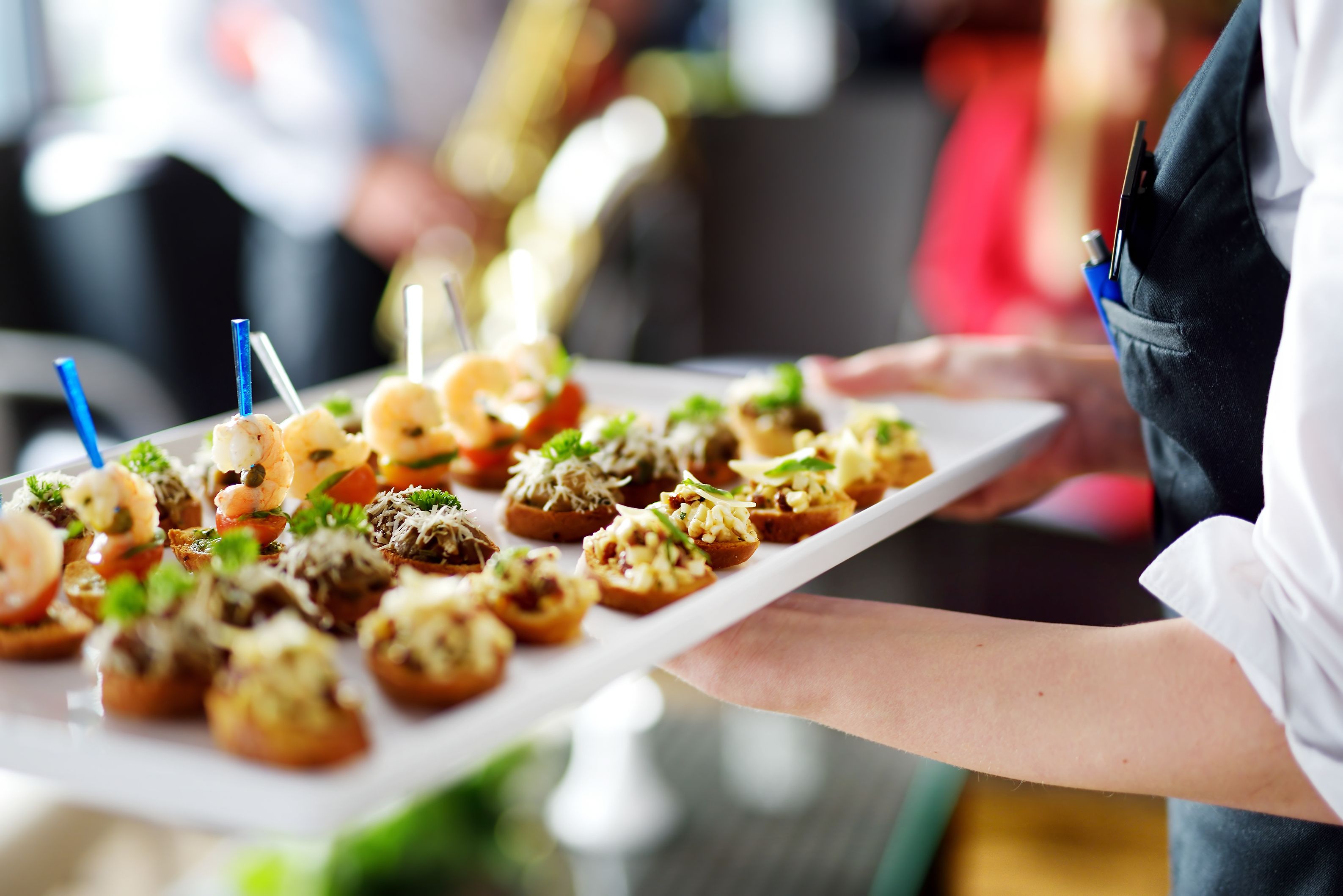 A tray of appetizers with various toppings, held by a person in a white shirt.