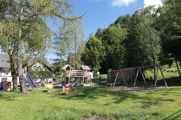 A playground with a wooden playhouse, slides, and swings. - Landgasthof Hasenstrick (Duernten)