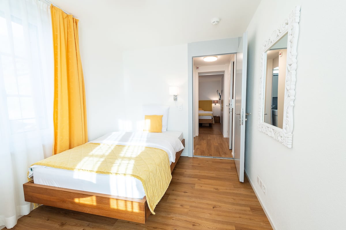 Un dormitorio con una cama de madera, una colcha amarilla y una pared blanca.