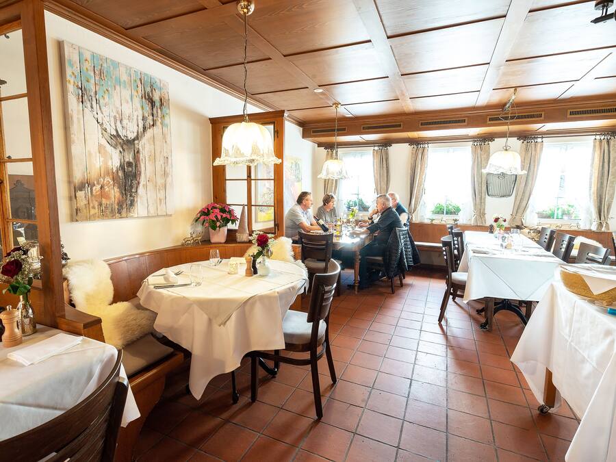 Un restaurante con mesas redondas, sillas de madera y un techo alto con vigas a la vista.