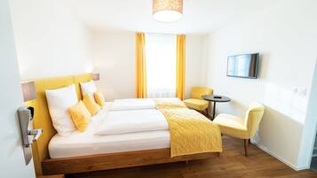 Een hotelkamer met een houten bed, gele beddengoed, een klein rond tafeltje en een stoel.