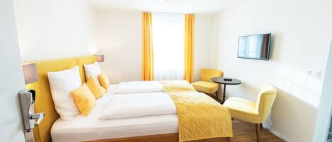 A hotel room with a wooden bed, yellow bedding, a small round table, and a chair.