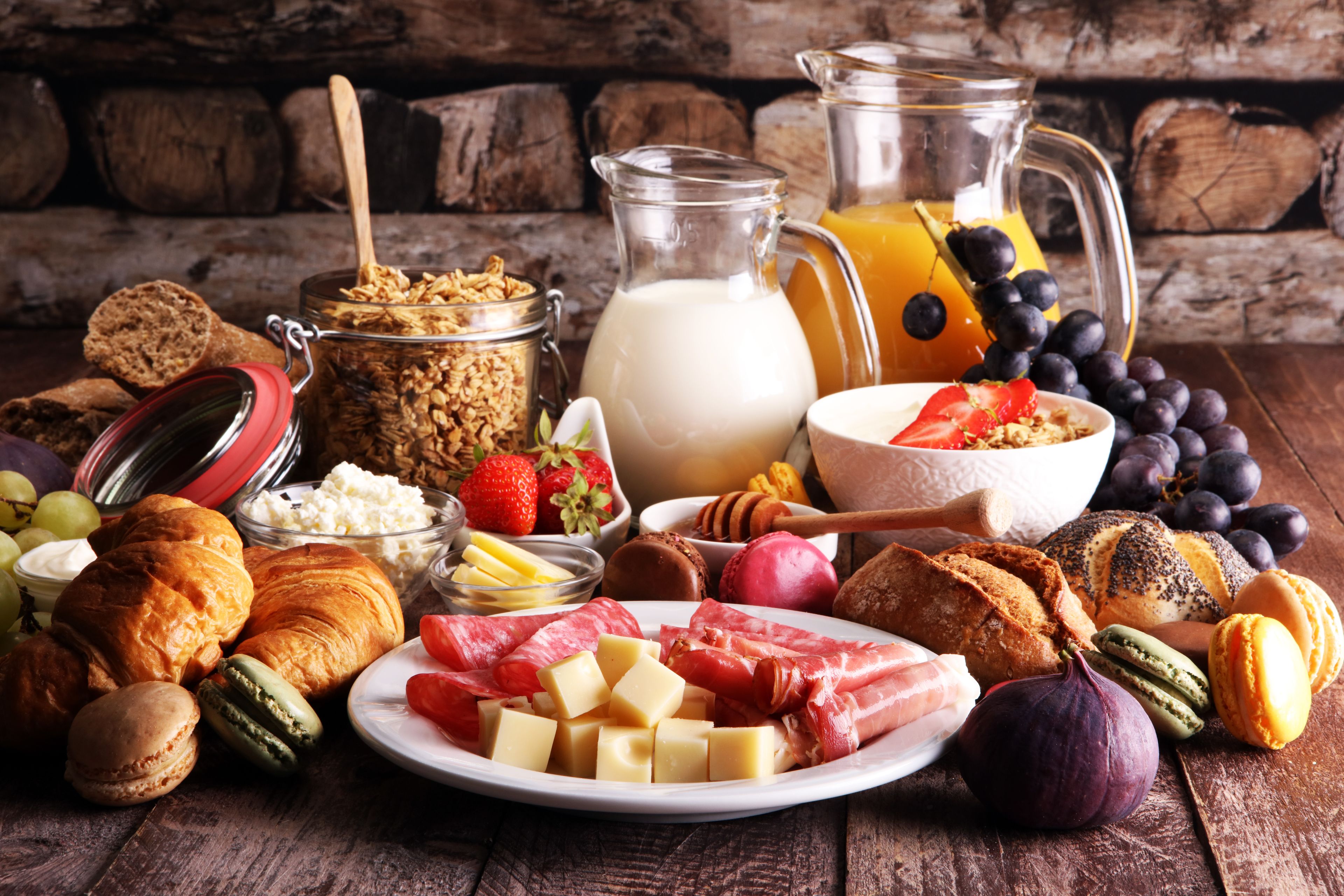 Une variété d’aliments, notamment du pain, du fromage, des fruits, et une cruche de lait, sont disposés sur une table en bois.