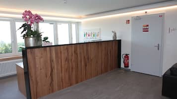 Un espace d’accueil avec un comptoir en bois, une plante en pot, un extincteur et une porte avec une pancarte.