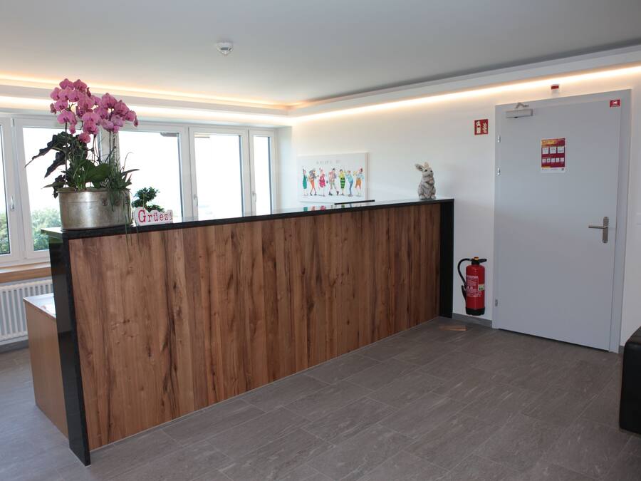Un espace d’accueil avec un comptoir en bois, une plante en pot, un extincteur et une porte avec une pancarte.