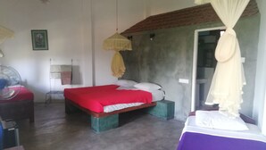 A bedroom with a bed, a standing fan, a bedside table, and a window with a curtain. - Tea Garden Holiday Inn (Ella)