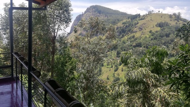 A view from a covered balcony overlooking a lush valley with a prominent hill in the distance. - Tea Garden Holiday Inn (Ella)