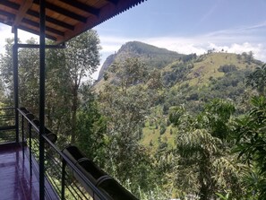 A view from a covered balcony overlooking a lush valley with a prominent hill in the distance. - Tea Garden Holiday Inn (Ella)