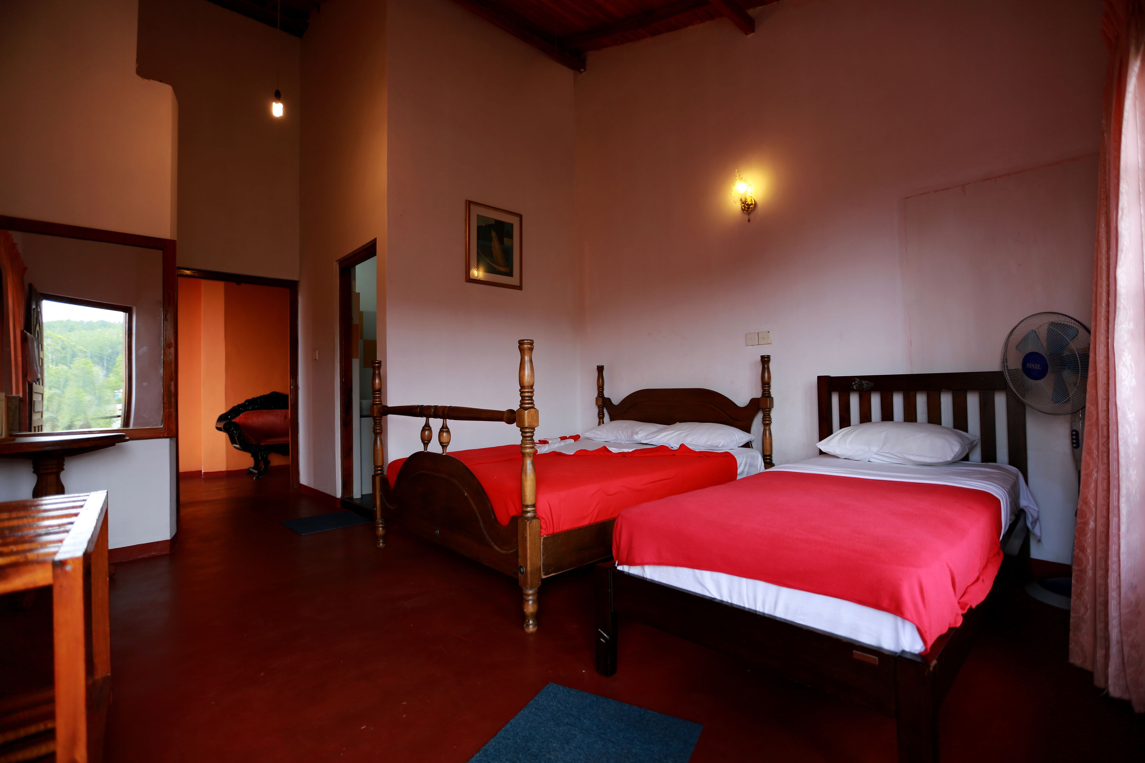 A room with two wooden beds, a wooden table, a chair, a fan, and a window with a view.