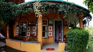 A yellow building with a curved roof, covered in greenery, and a small porch area with chairs. - Tea Garden Holiday Inn (Ella)