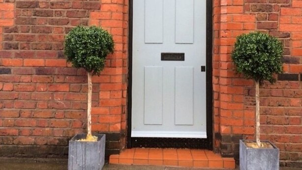 A brick building with a white door, two potted plants, and a small sign above the door. - The Liverpool Pod - Hostel (Liverpool)