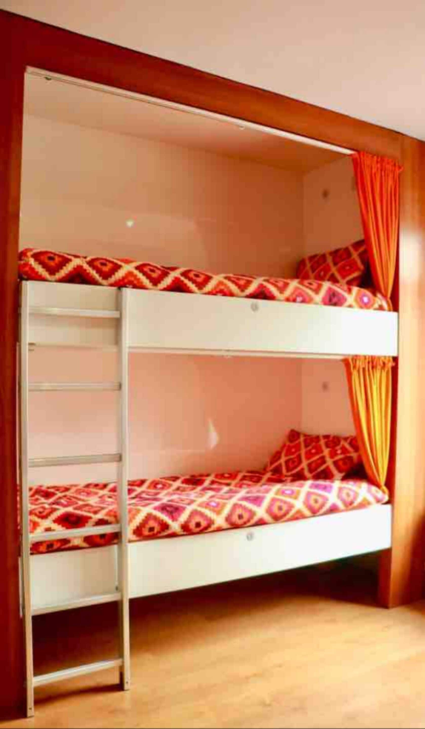 Una cama litera con escalera, ropa de cama estampada y cortinas naranjas.