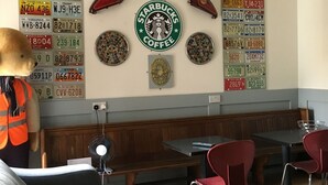 A restaurant interior with a booth seating area, a large wall display of license plates, and a Starbucks Coffee sign. - The Liverpool Pod - Hostel (Liverpool)