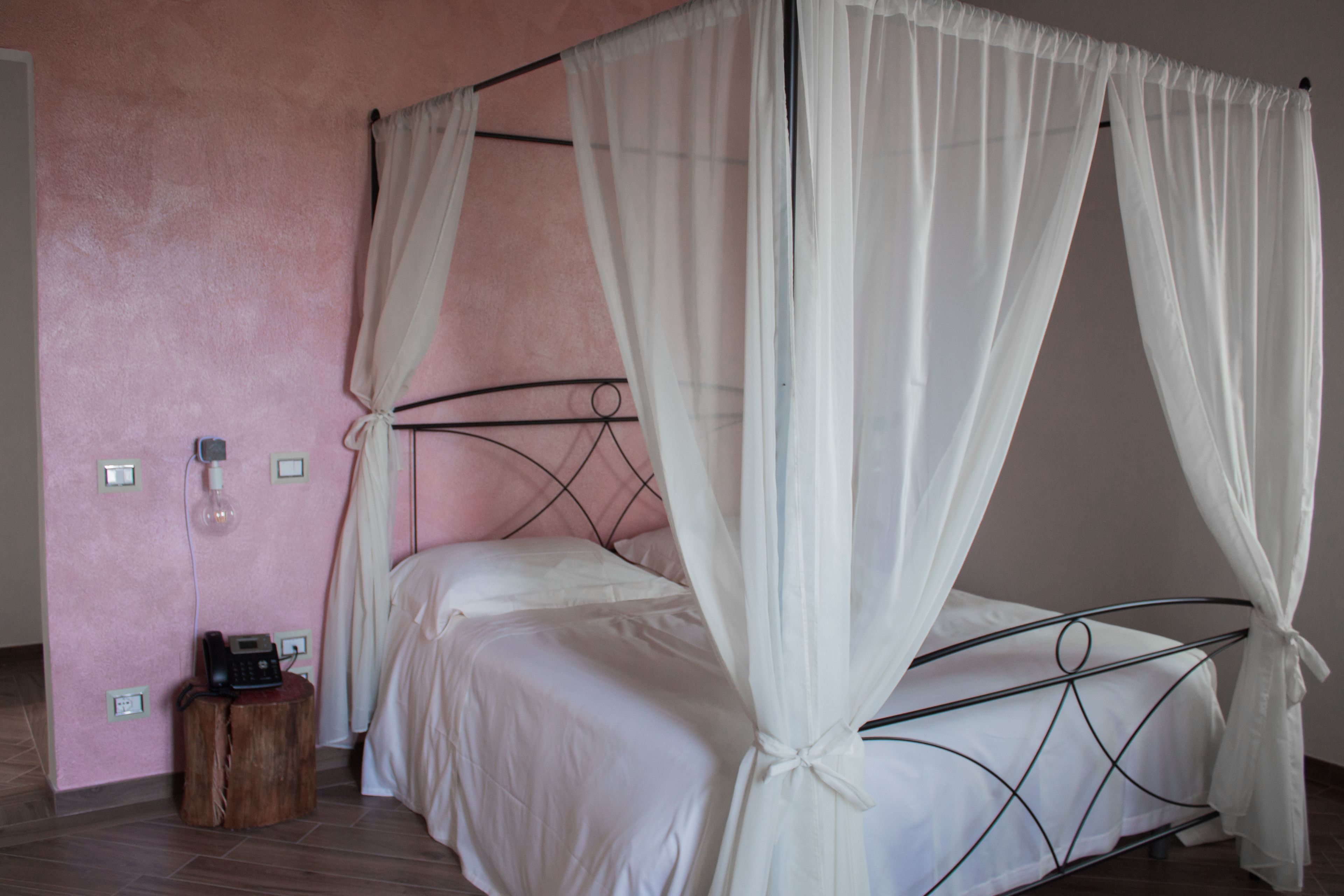 A single bed with a metal frame and white bedding, a bedside table with a lamp, and a power outlet on the wall.