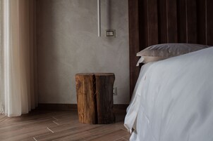Un dormitorio con suelo de madera, una mesita de noche y una cama con ropa blanca.