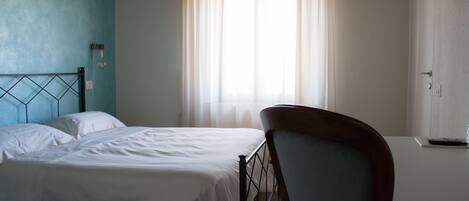 A bedroom with two beds, a wooden chair, a bedside table, and a window with curtains.