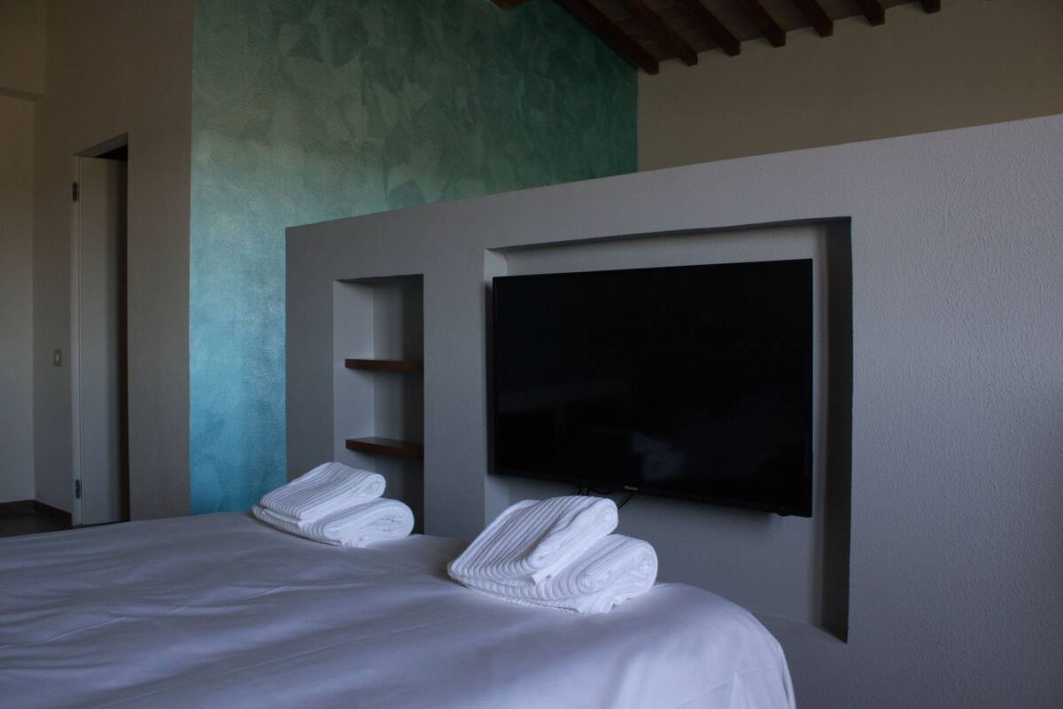 Une chambre d’hôtel avec un lit, un téléviseur fixé au mur et une porte donnant sur une autre pièce.