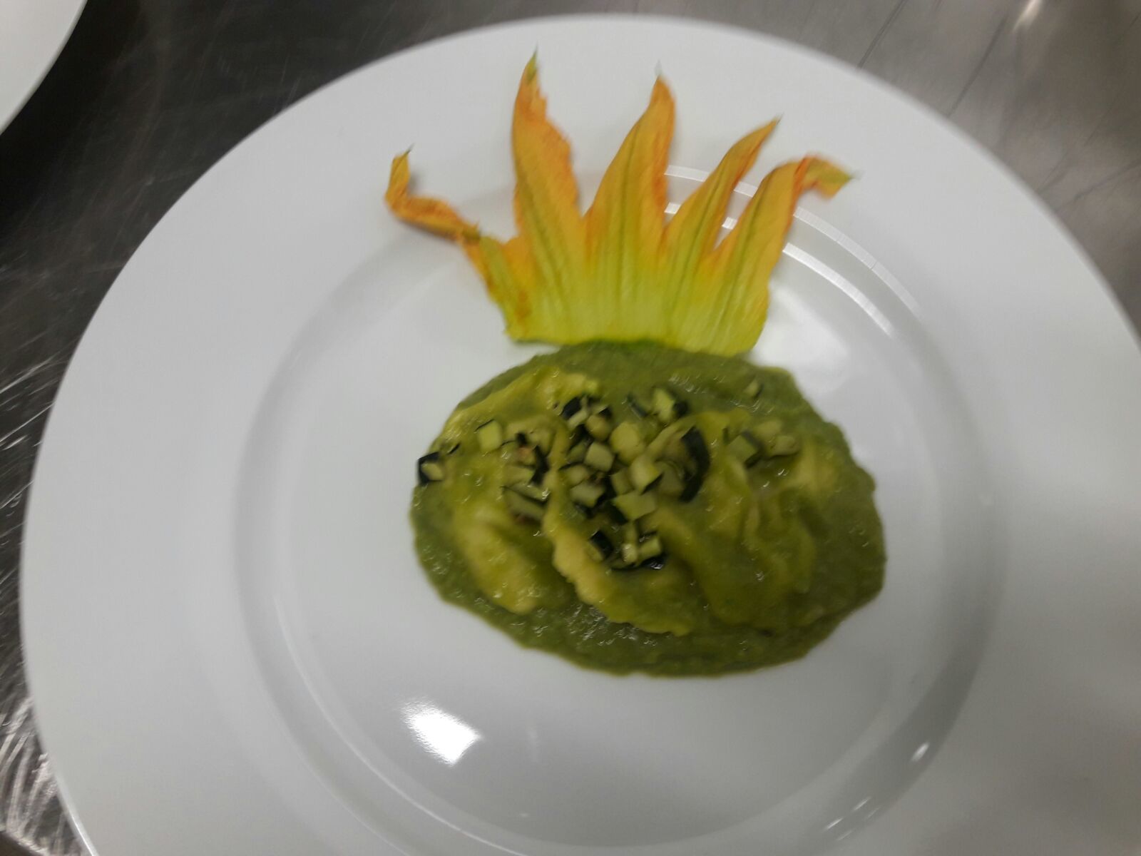 A white plate with a green dish topped with diced ingredients, possibly a vegetable or meat dish, and a decorative orange garnish.