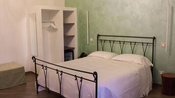 Una cama individual con estructura metálica, una mesita de noche, un perchero y un taburete pequeño.