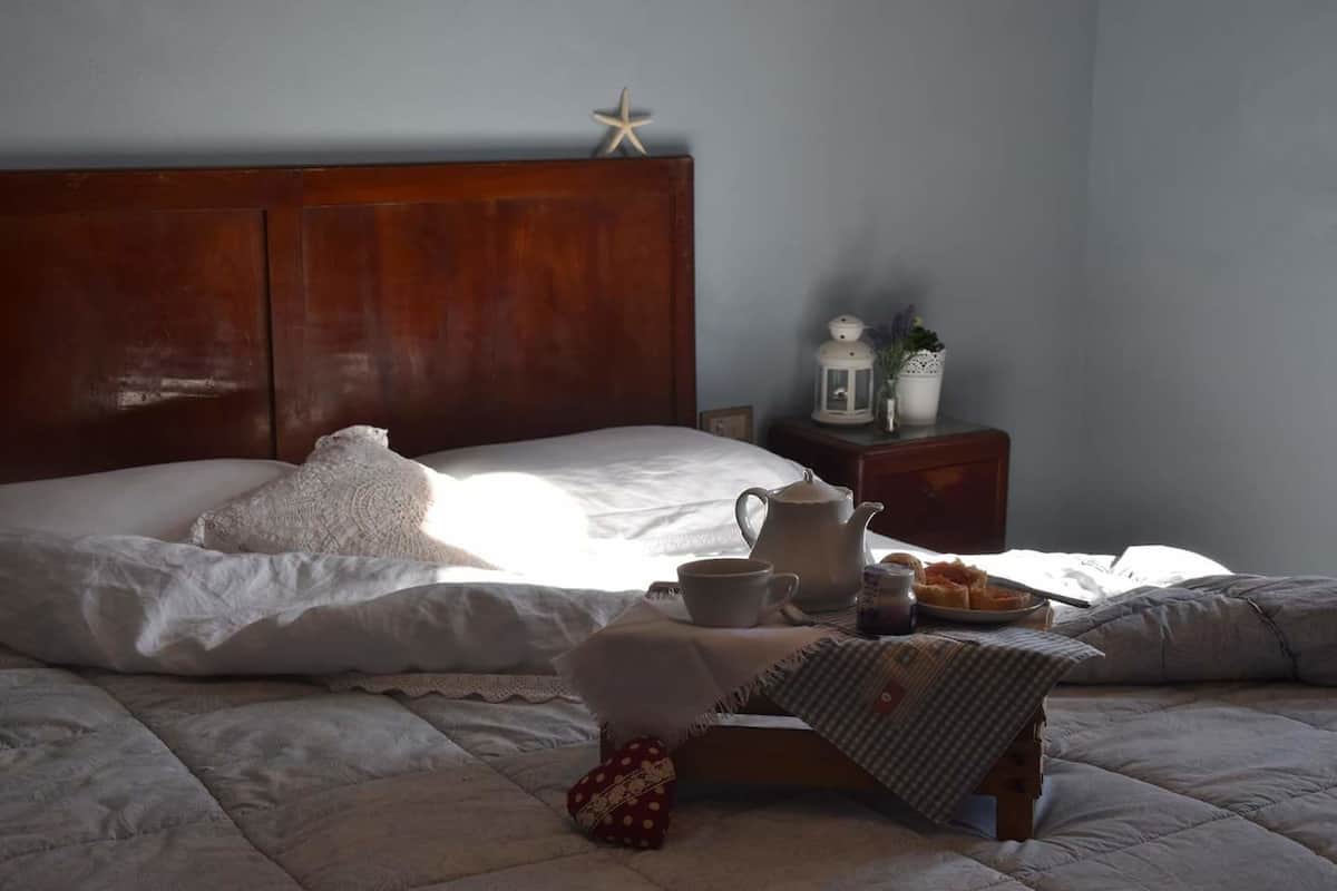 A neatly made bed with a starfish decoration, a bedside table with a lantern, a kettle, and a plate of pastries.