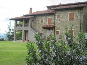 A stone building with a red-tiled roof, a balcony, and a grassy lawn.