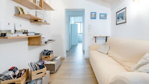A modern living room with a beige sofa, wooden shelves with books and plants, and a hallway leading to another room. - B&B Mimosa e Lillà (Fumane)