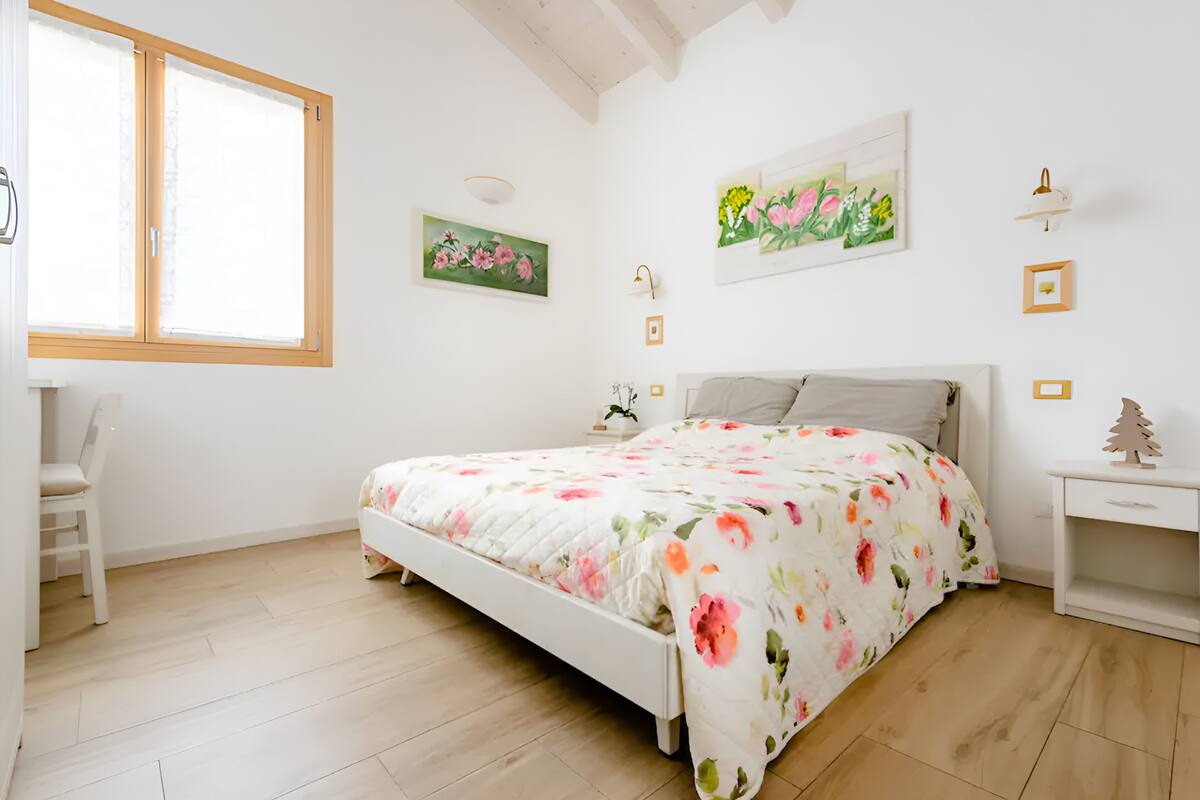Un dormitorio con cama, una silla, una mesita de noche y una ventana.