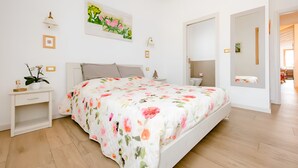 A bedroom with a bed, bedside tables, a nightstand, a wall-mounted lamp, and a painting. - B&B Mimosa e Lillà (Fumane)