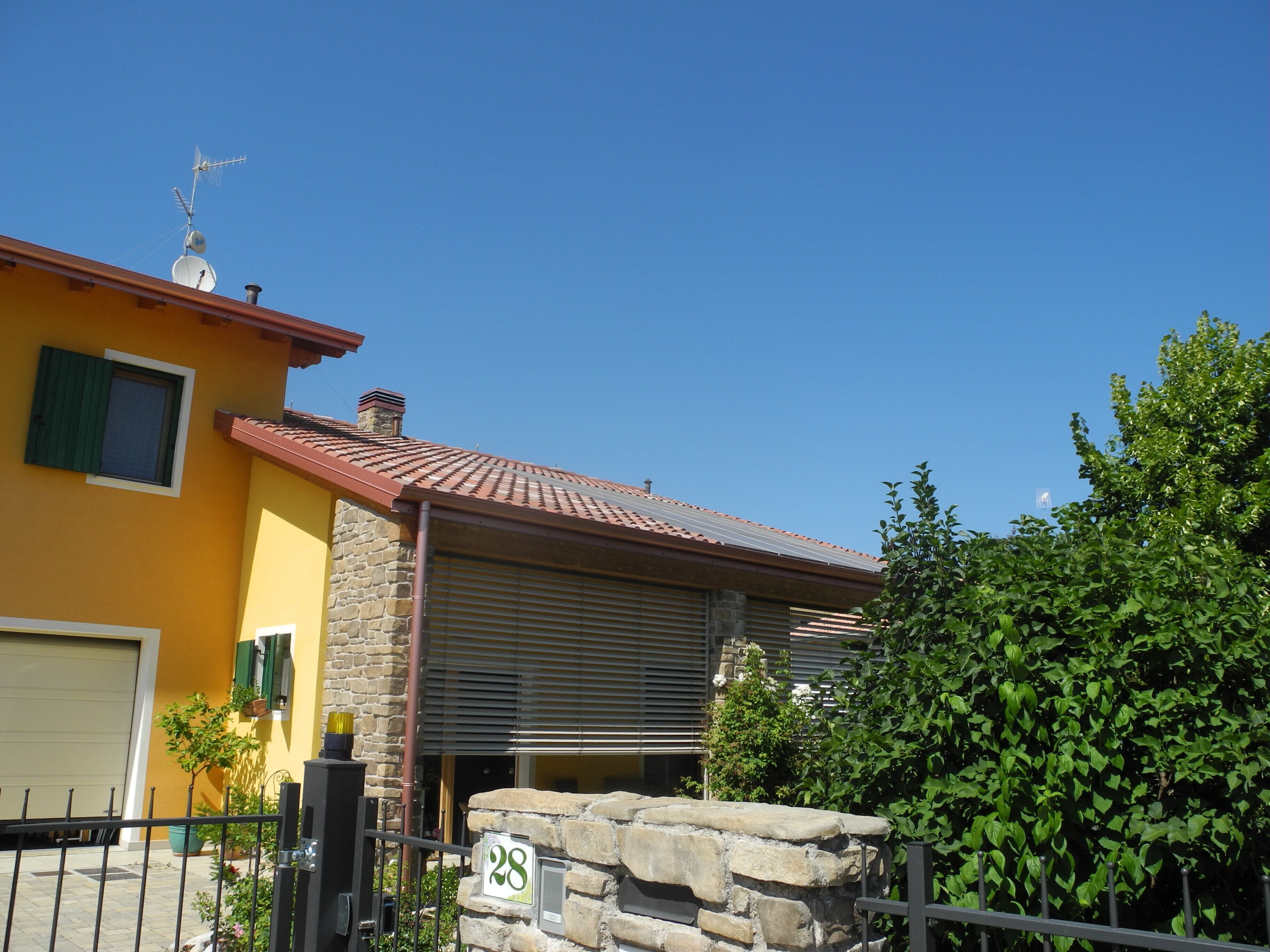 Un bâtiment jaune avec une façade en pierre, un toit recouvert de tuiles rouges et une enseigne portant le numéro 28.