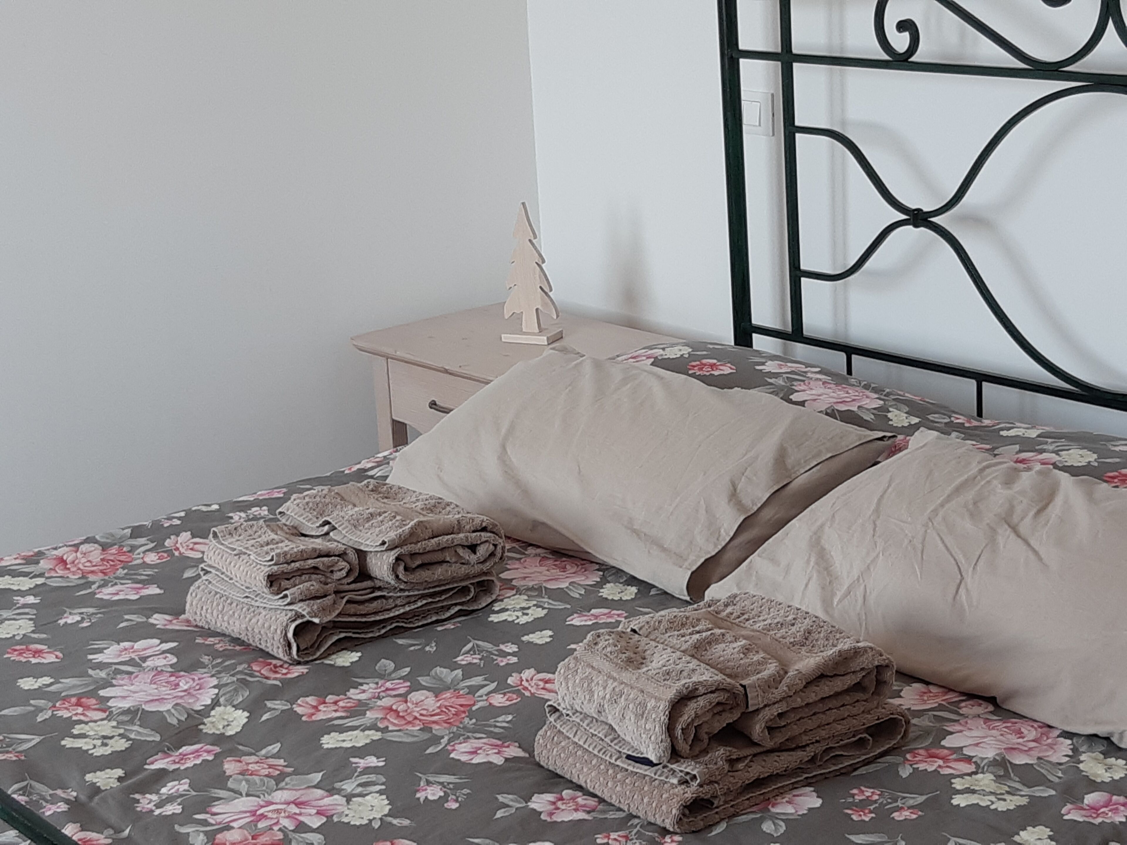 A neatly made bed with floral bedding, a bedside table with a lamp, and a decorative tree.